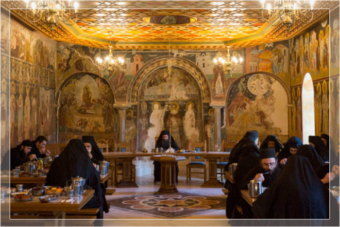 Монахи едят в трапезной монастыря Пантократор на Афоне, Греция, в окружении византийского искусства.