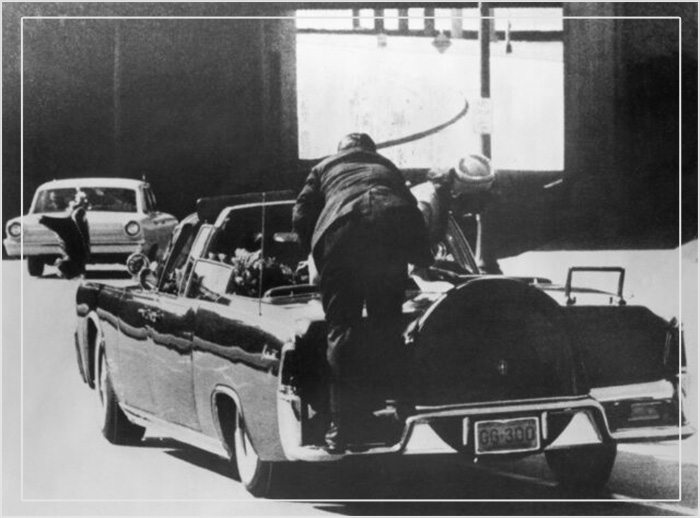 Первая леди Жаклин Кеннеди склоняется над раненым президентом США Джоном Кеннеди, а к ним мчится агент Секретной службы. 