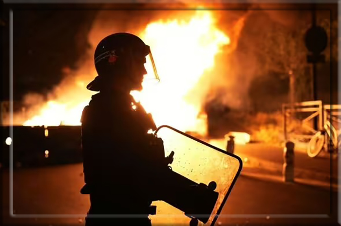 Пожарный наблюдает, как горят автомобили после беспорядков в Нантере, к западу от Парижа.