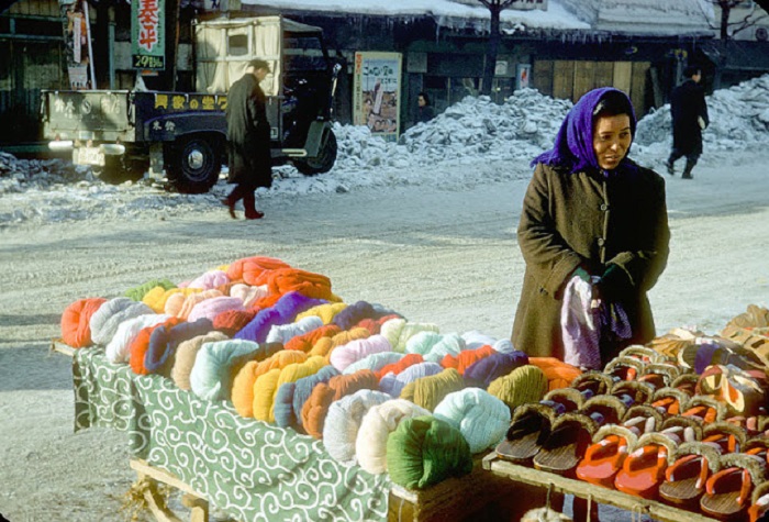 Женщина торгует зимними тапочками и платками прямо на деревянном лотке.