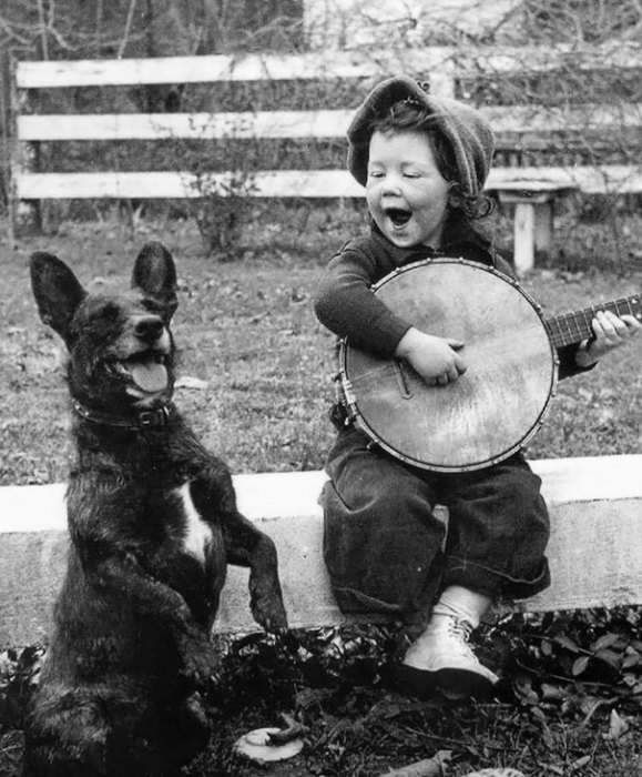 Девочка играет на банджо для своей собаки.