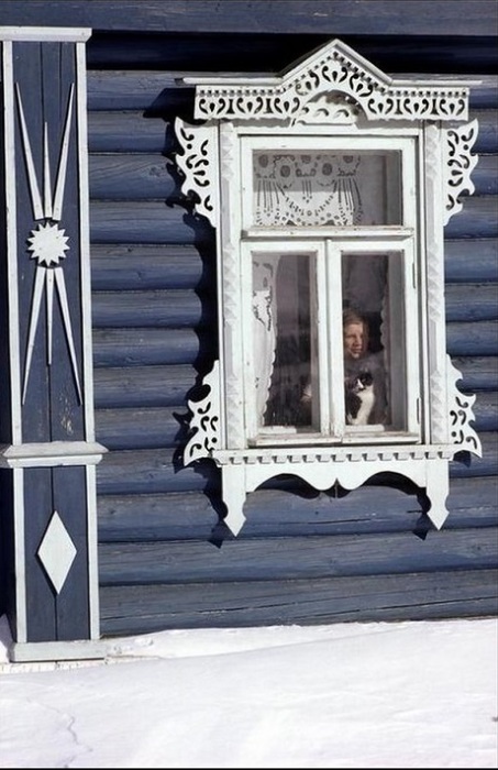 Мальчик с котом выглядывают из окна русской избы.