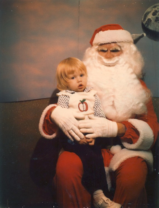 Упитанный рождественский дедушка держит девочку на коленях.