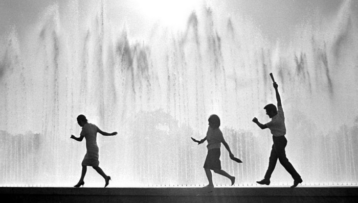 Молодые люди получают удовольствие бегая босиком по бордюру фонтана, ловя брызги воды.