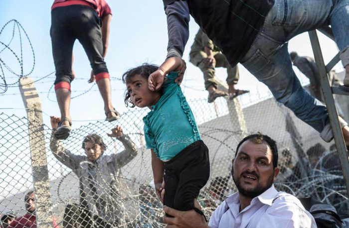 Беженцы перелезают через забор на границе Турции и Сирии.