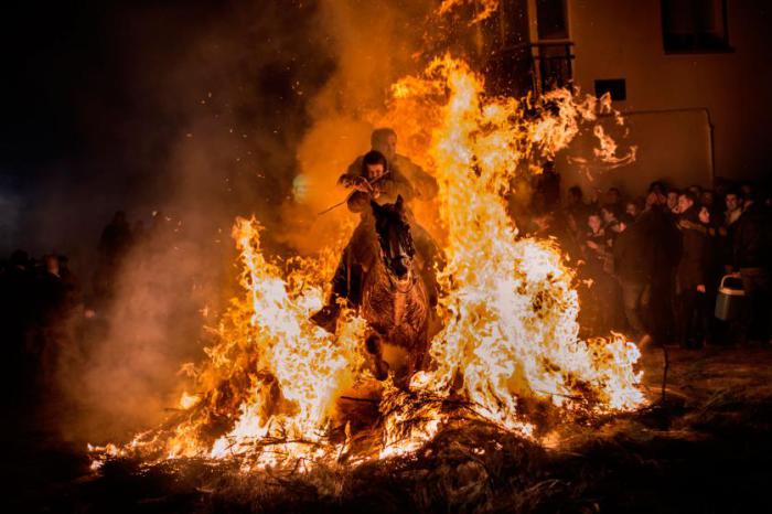 Мужчина с ребенком преодолевают огненную полосу препятствий во время ежегодного религиозного празднования «Luminarias» в ночь накануне Святого Антония — покровителя животных.