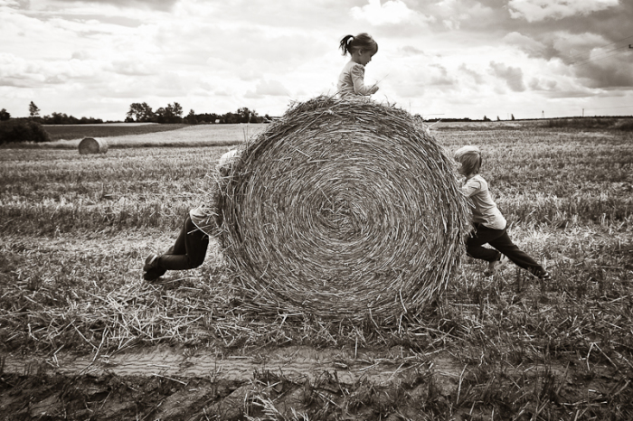 Ребята играются с огромнейшим стогом сена в поле.