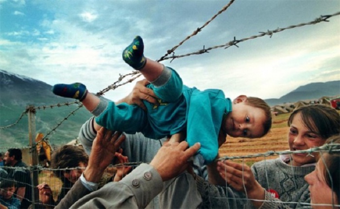 Двухлетнего мальчика передают родственникам через колючую проволоку во время кровавого конфликта в Косово.