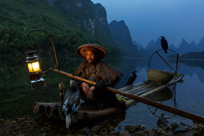 Китайский рыбак с обученными бакланами ждёт рассвета, чтобы начать рыбалку.