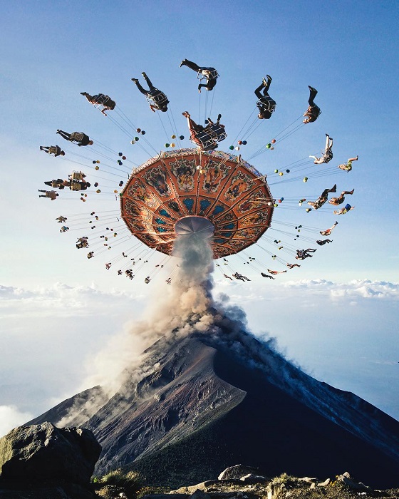 Разноцветная карусель на вершине вулкана, который выпускает клубы дыма.