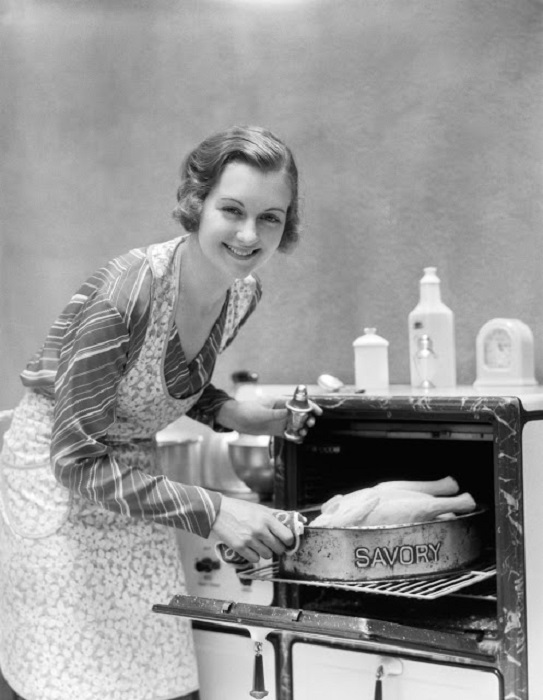 Хозяйка, с улыбкой на лице, отправляет курицу в духовку.