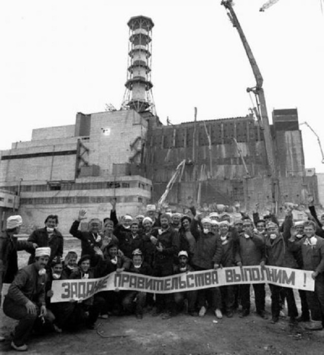Групповой снимок ликвидаторов на фоне изоляционного сооружения над четвёртым энергоблоком Чернобыльской атомной электростанции. Украина, Чернобыль, 1986 год. 