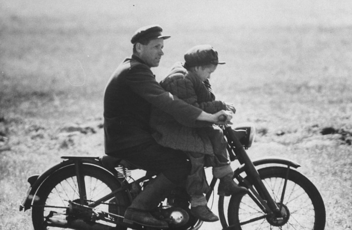 Колхозник с сыном катающийся на старом мотоцикле.