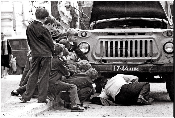 Группа подростков рядом с мужчиной, ремонтирующим автомобиль. 
