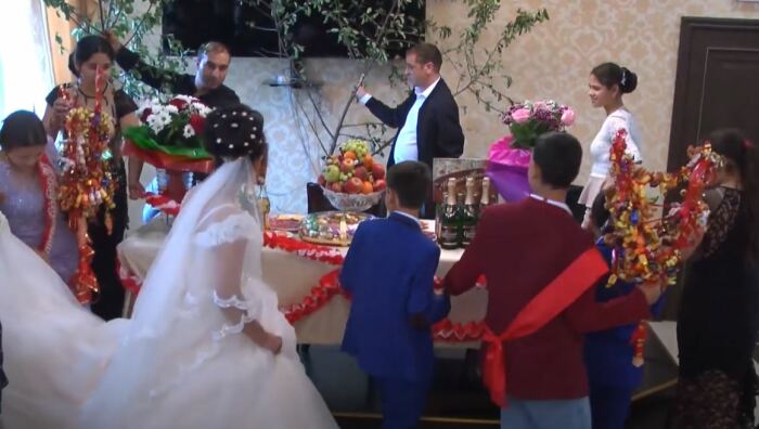 Жених, невеста и родня обходят свадебный стол с деревцами с знак будущего финансового благополучия молодой семьи. Видеокадр