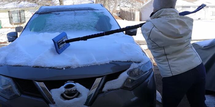 Тиша чистит машину от снега ногами. /Видеокадр