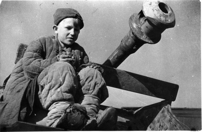 Советский подросток сидит у ствола брошенного при немецком отсуплении артиллерийского орудия. 